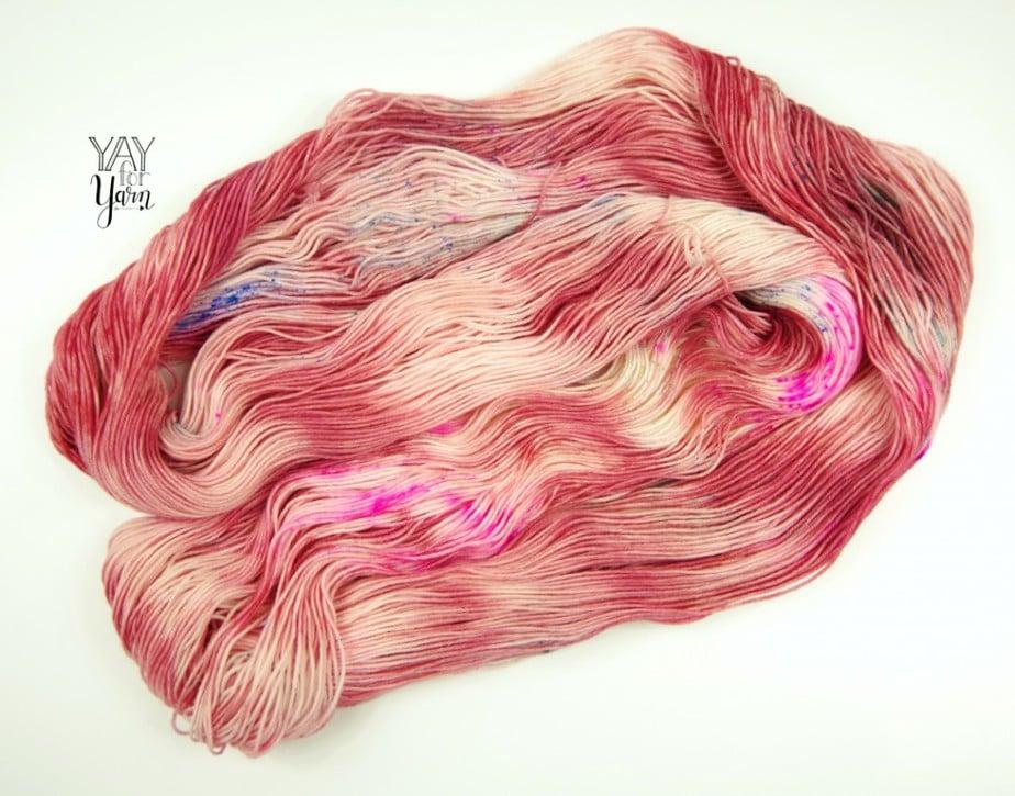 a puddle of hand dyed merino wool sock yarn in pink, rose, and neon speckles