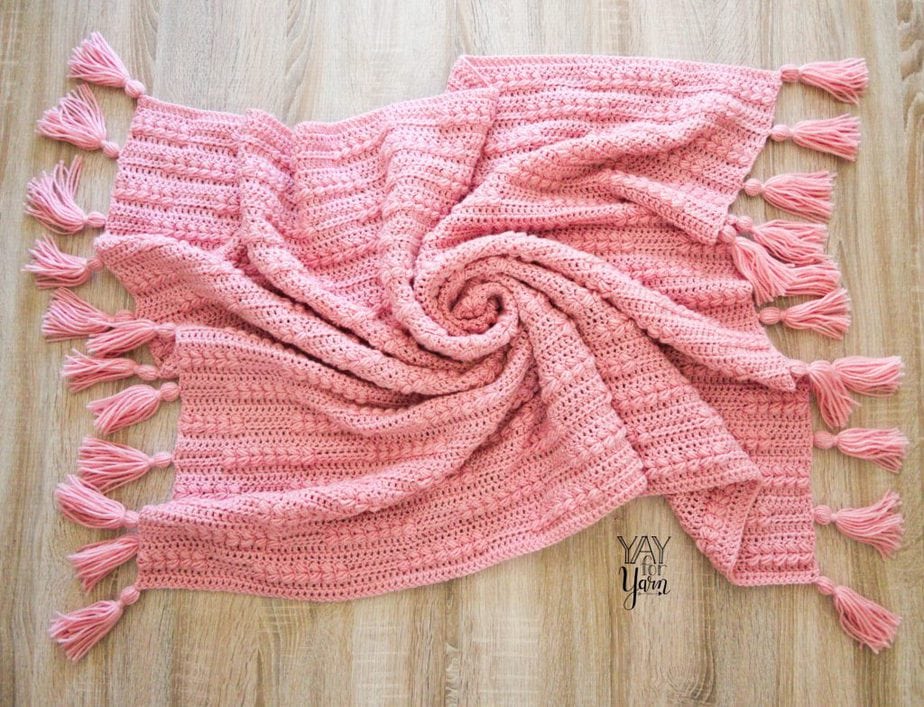 pink crocheted blanket with tassels swirled on the floor