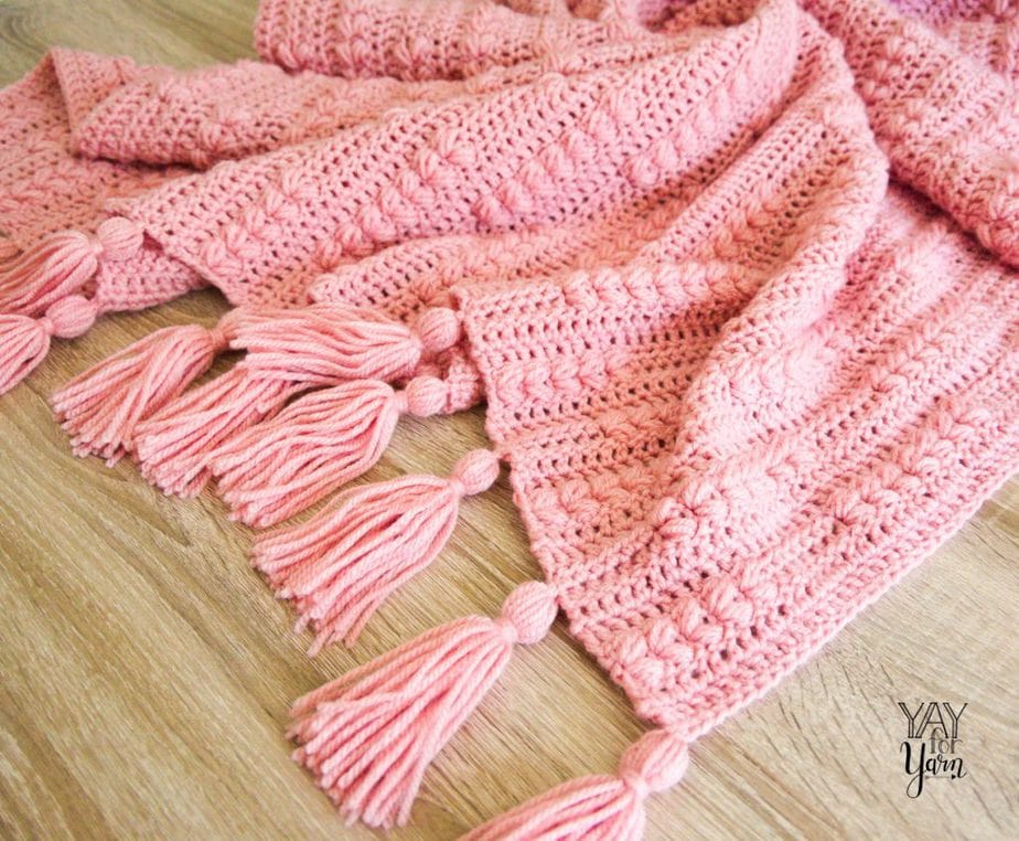 pile of pink crochet blanket with tassels on wood floor