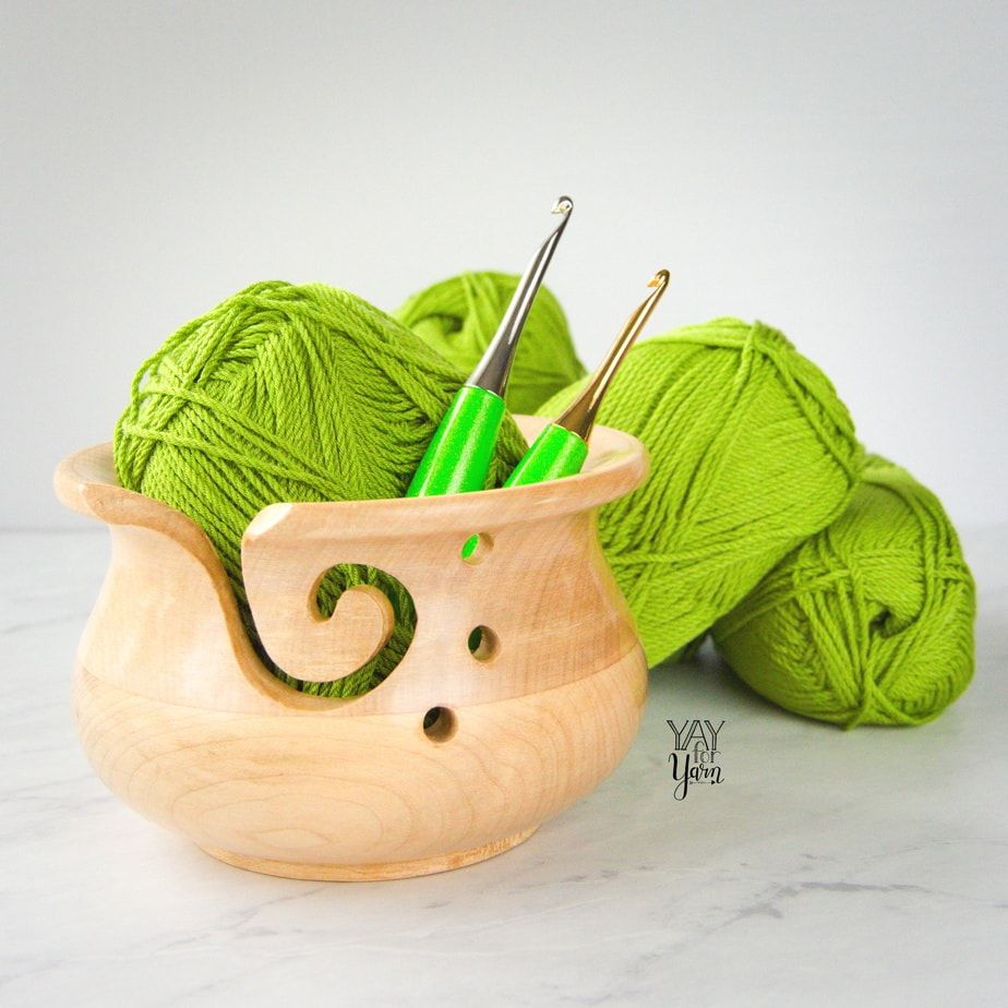 two furls odyssey lime crochet hooks in wooden yarn bowl on marble counter, with lime green skeins of yarn in background