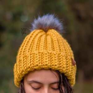 Close-up of a girl outdoors wearing yellow crochet ski hat with gray fur pom pom