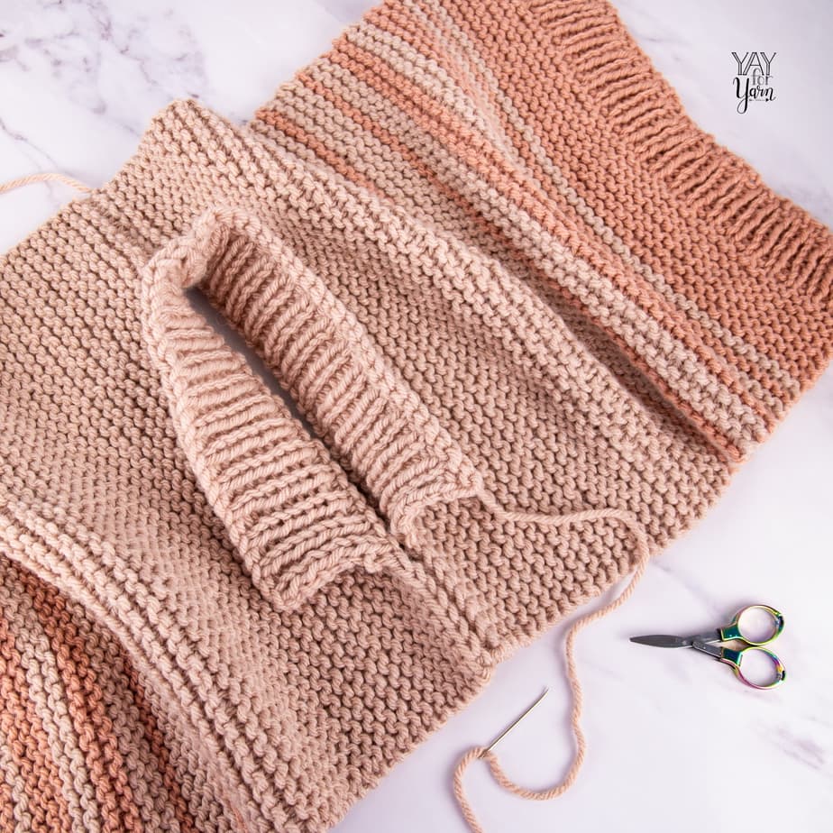 work in progress - seaming shoulders of beige and terracotta dip dye knitted pullover sweater on white marble with metal scissors