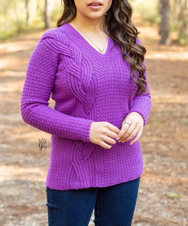 woman wearing purple v-neck sweater with large braid on one side standing in forest