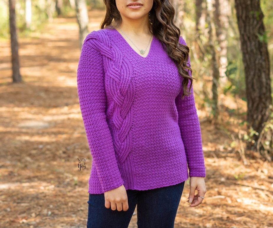 woman wearing purple v-neck sweater with large braid on one side standing in forest