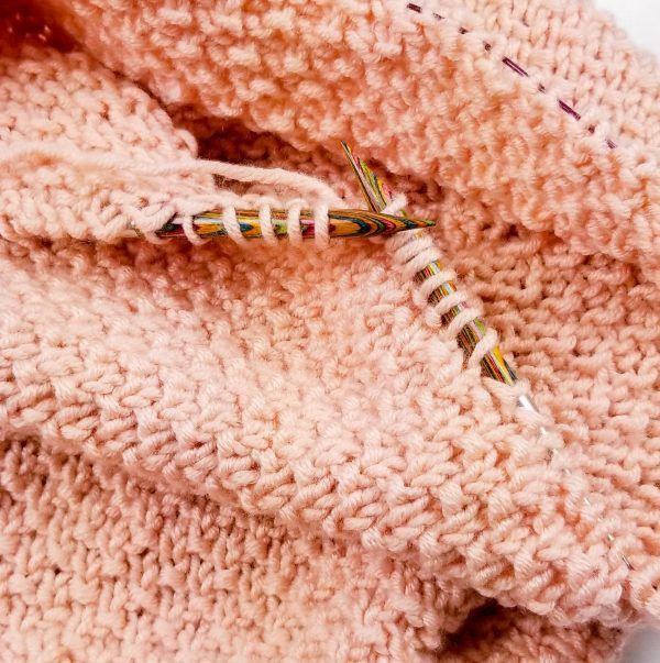 Into the pink yarn are the knitting needles in gold