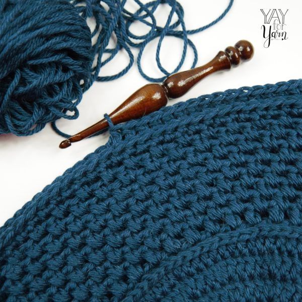 A dark brown wood crochet hook and a dark blue yarn in a white background