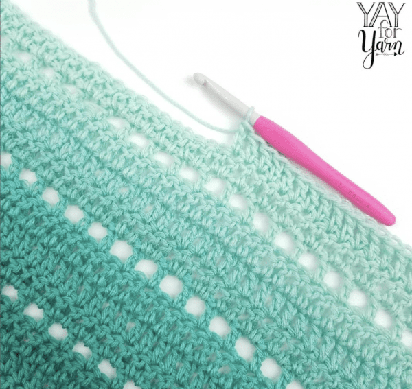 Into the seafoam colored yarn is a crochet silver hook with metallic pink handle in white background