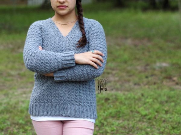front view of a girl outdoor wearing a gray textured pullover crochet sweater and light pink jeans