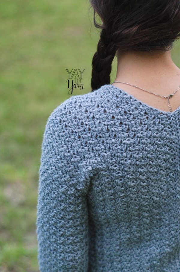 the back of a girl outdoors wearing a gray textured pullover crochet sweater and a silver necklace